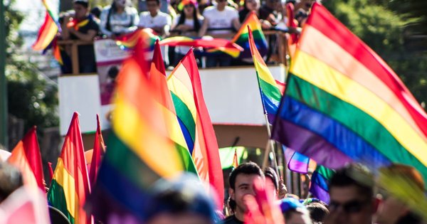 A large Pride crowd waving rainbow flags in a European city square