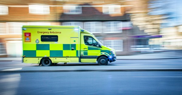 A blurred NHS ambulance responding on a London street