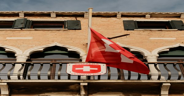 Swiss flag flying against a blue sky in front of a government building