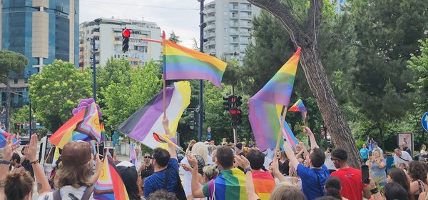 Rainbow and trans Pride flags flying against the Tirana skyline