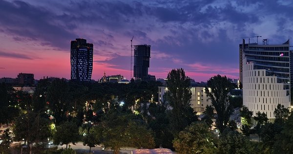 A pride rainbow flag waving on a balcony with a European city skyline behind it