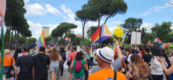 Marchers carrying Progress Pride flags down a tree-lined boulevard in central Tirana